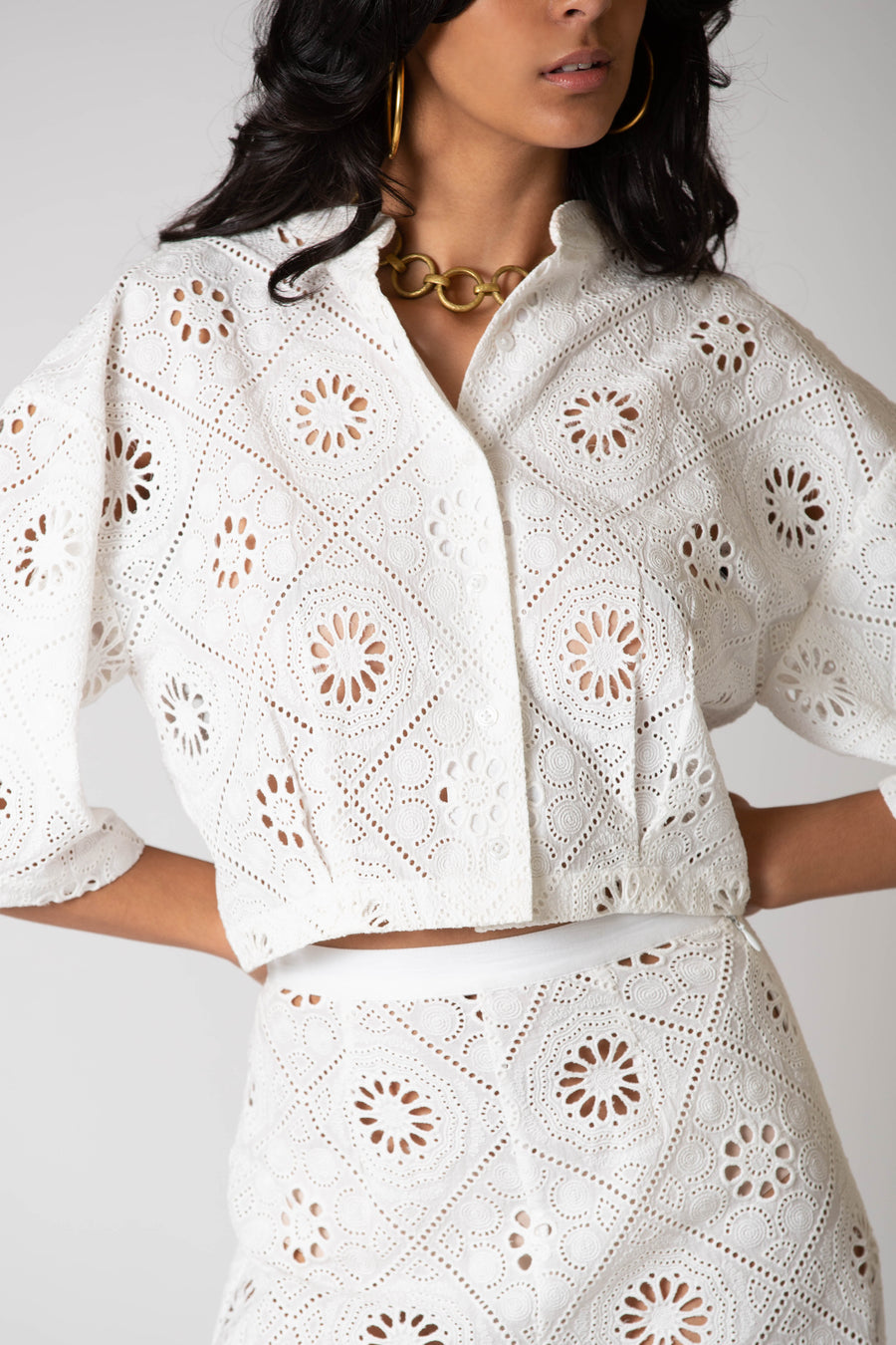 This is a close-up photo of a woman posing in matching, white embroidered top and pants.