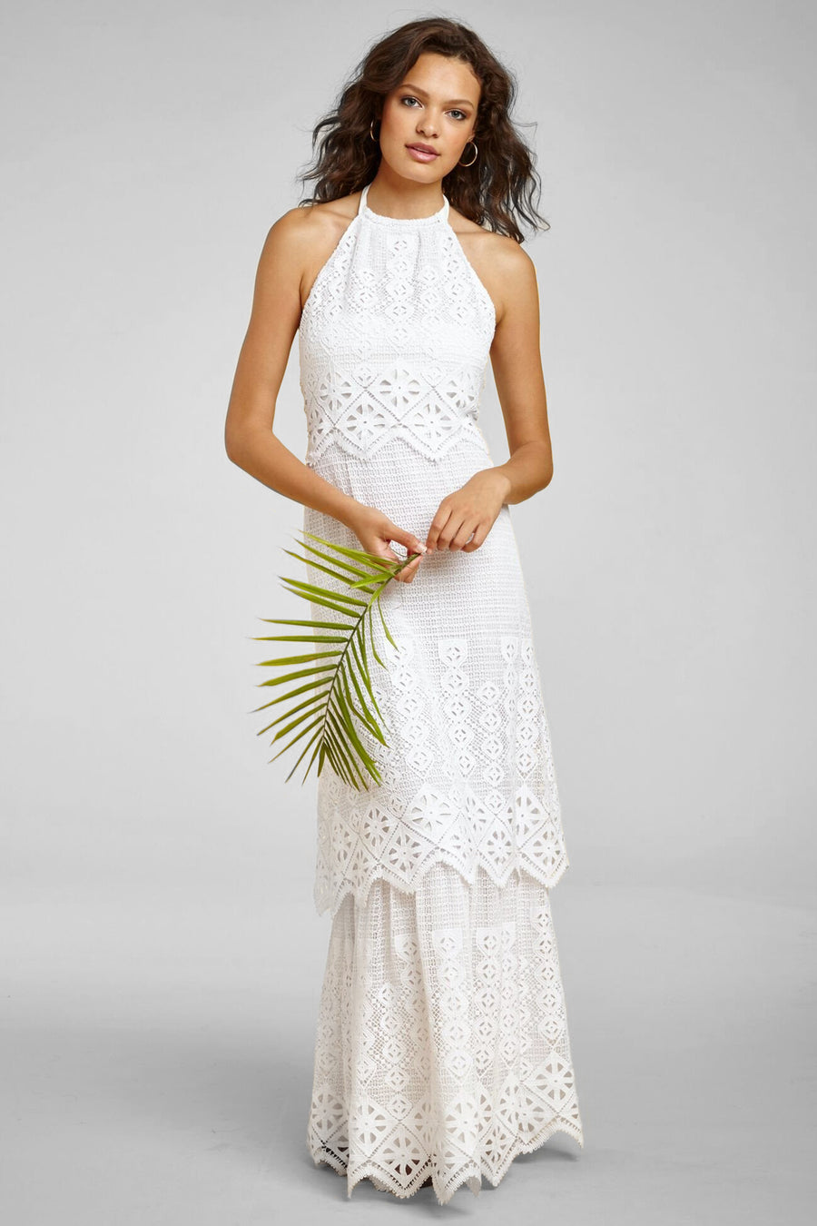 This is a photo of a woman wearing a long white halter dress. She holds greenery in her hands.