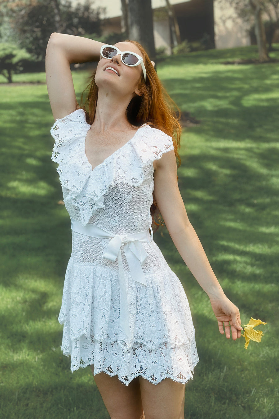 This is a photo of a woman wearing a white, lace dress with layered ruffles that end above the knee.