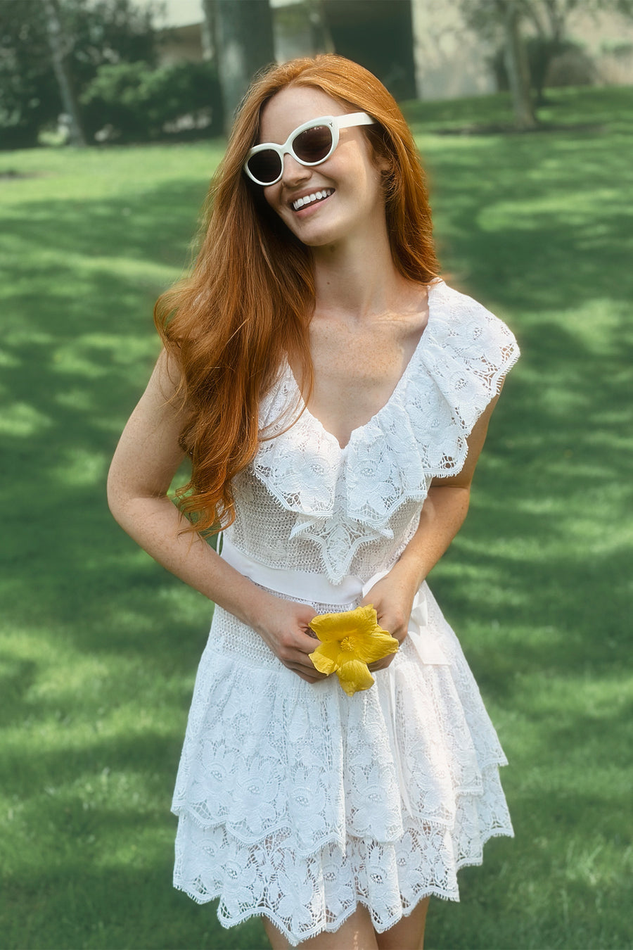 This is a photo of a woman wearing a white, lace dress with layered ruffles that end above the knee.