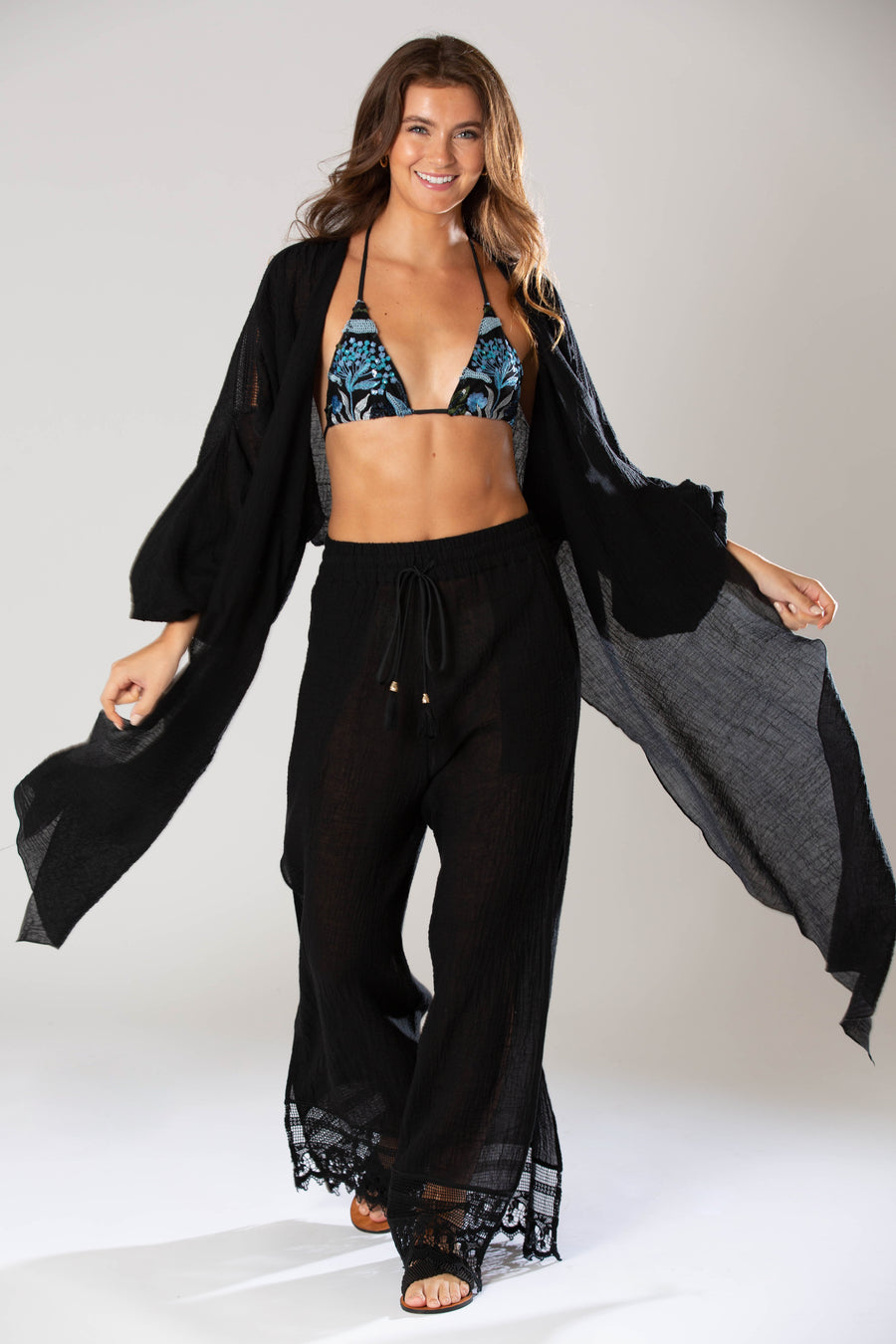 This is a photo of a woman posing in a bikini top, wearing black pants and kaftan over it.