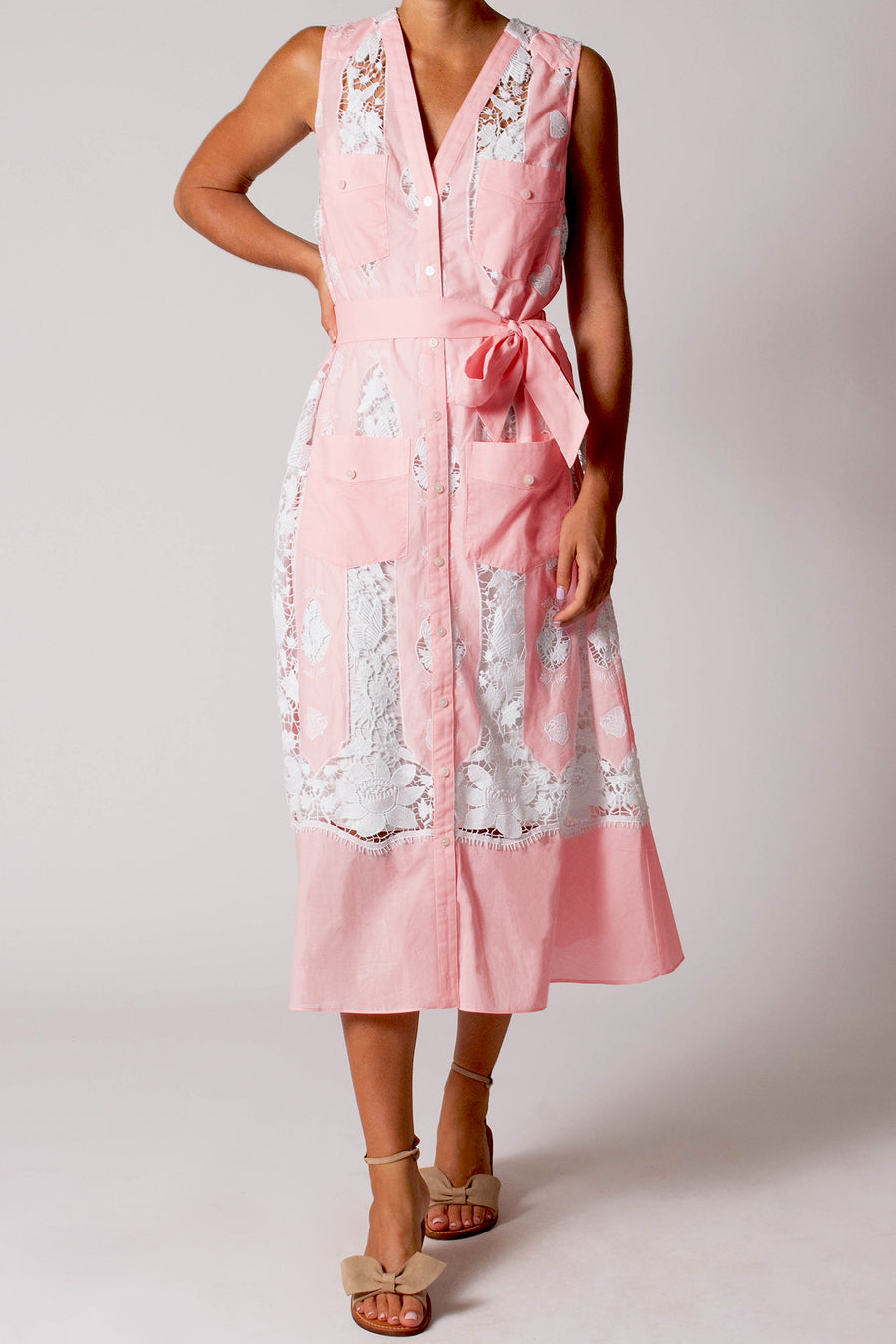 This photo shows a woman wearing a long pink dress with pockets and lace detailing. It has a V- neckline and buttons that go down the front of the dress.