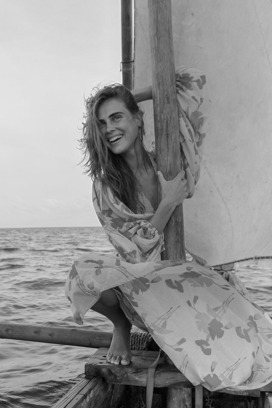 This is a black and white photo of a woman on a boat wearing a long flowy dress.