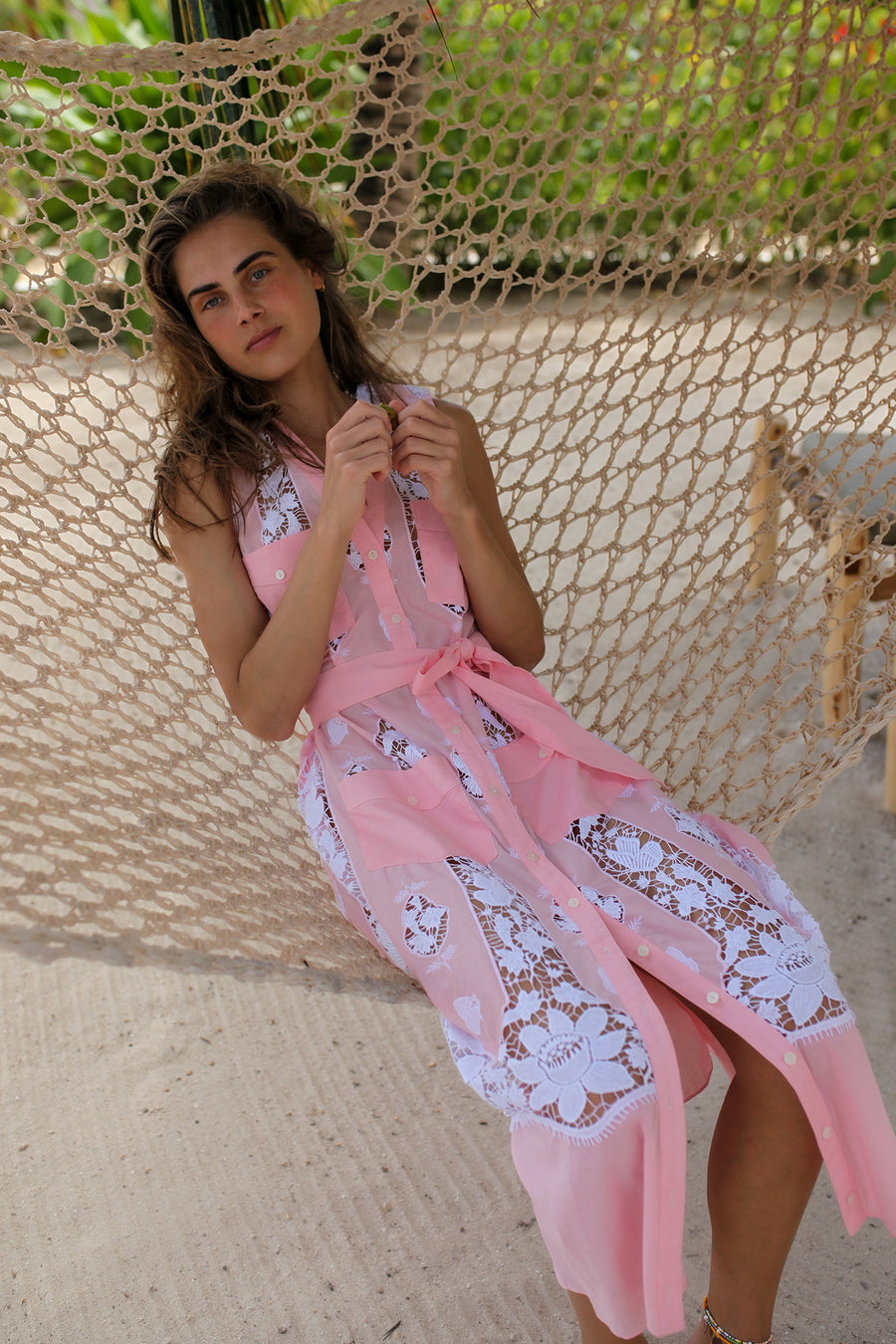 This photo shows a woman laying on a hammock wearing a bubblegum pick dress with lace detailing and pockets.