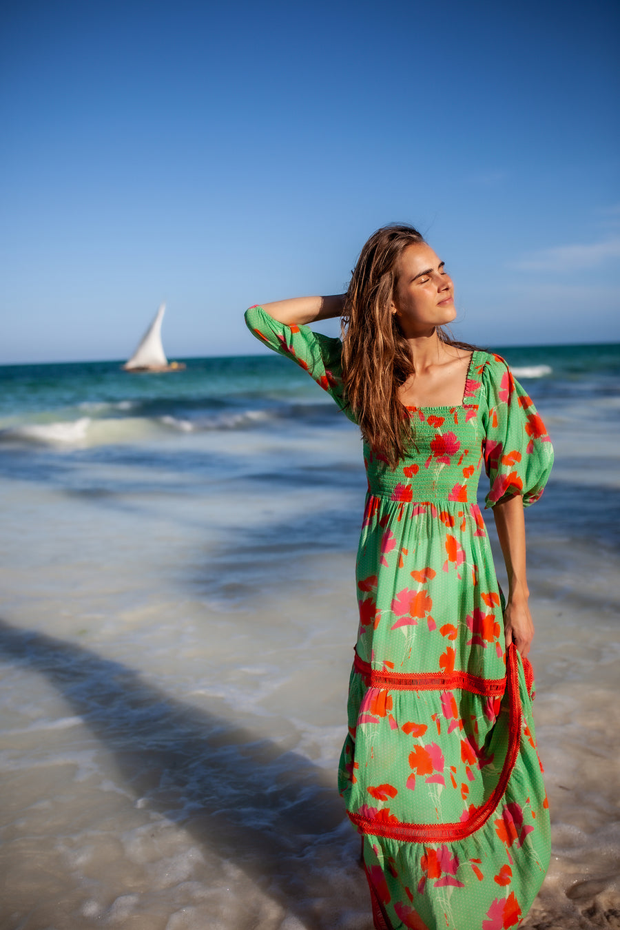 This is a photo of a woman wearing a long green printed dress on the beach.