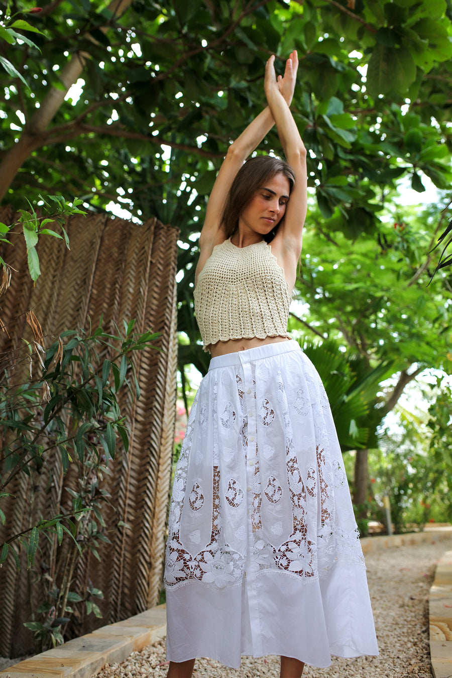 This is a photo of a woman wearing a long white skirt with lace detailing. There are buttons that go down the center and lace that creates an intricate pattern around. 