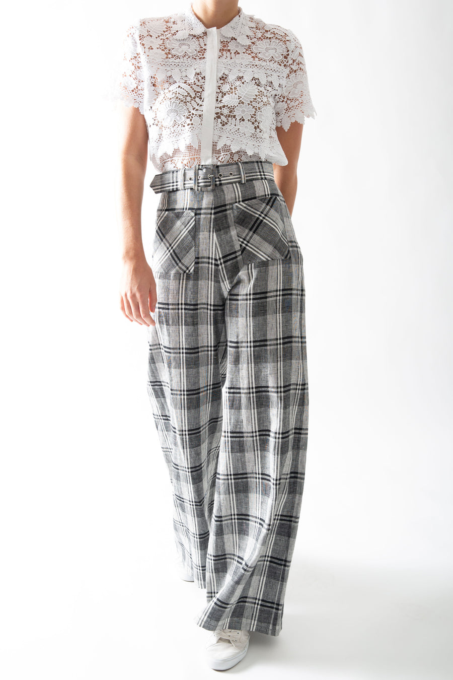 This is a photo of a woman from the neck down, she is wearing a lace, collared, button front top tucked into plaid wide leg pants. The top is a detailed floral lace embroidery, with leaf shaped scallops throughout.