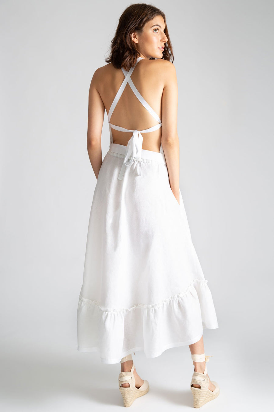 This is a photo of the back of a solid white linen dress. The back features an open criss-cross look with gross grain ribbon and side pockets on seam.