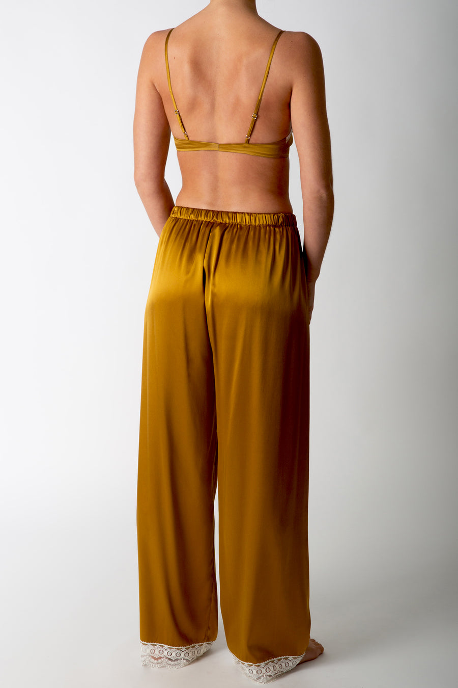 This is a back side photo of a woman wearing a silk gold bralette with matching pants.