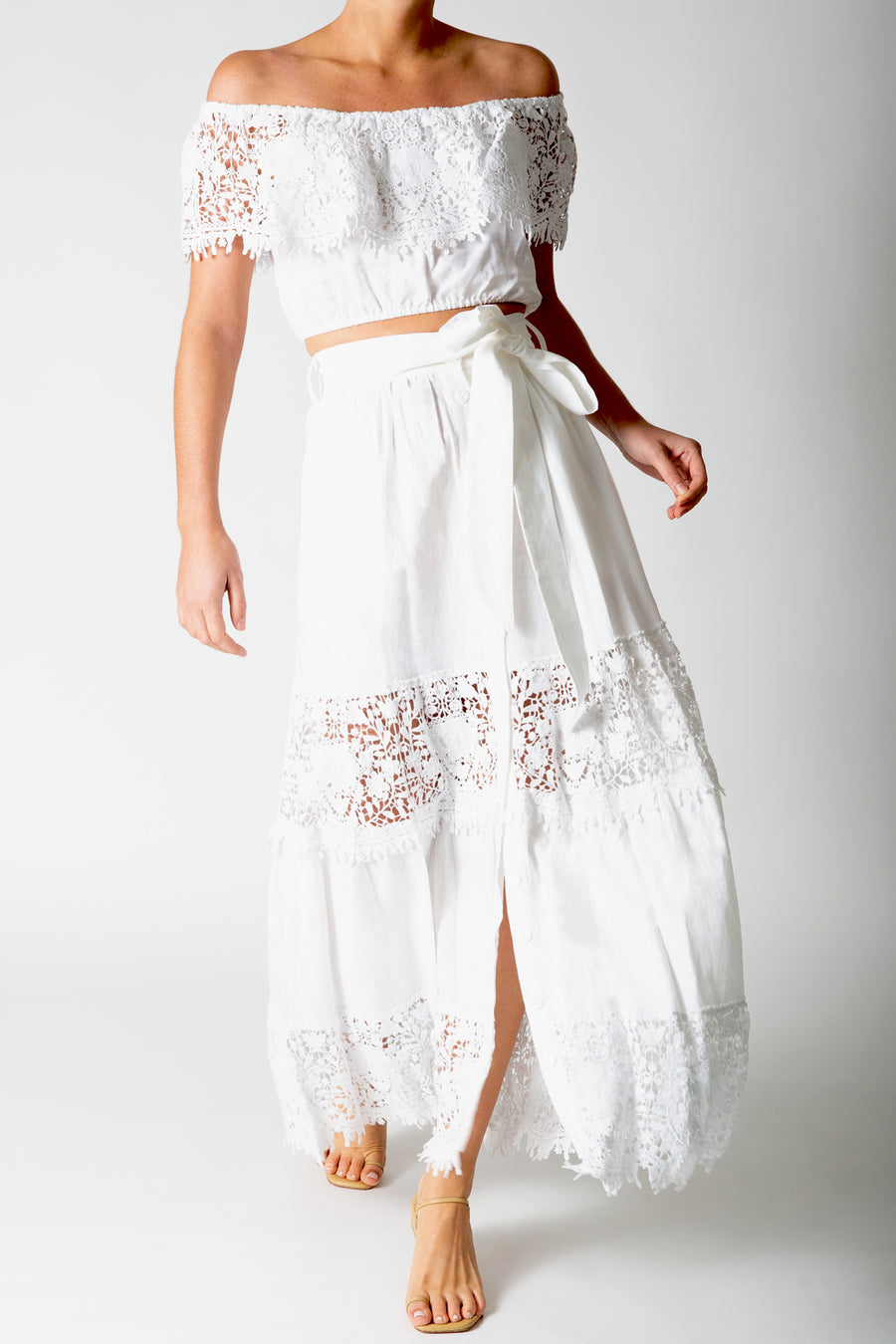 This is a photo of a woman wearing a white lace crop top with a matching white maxi skirt.