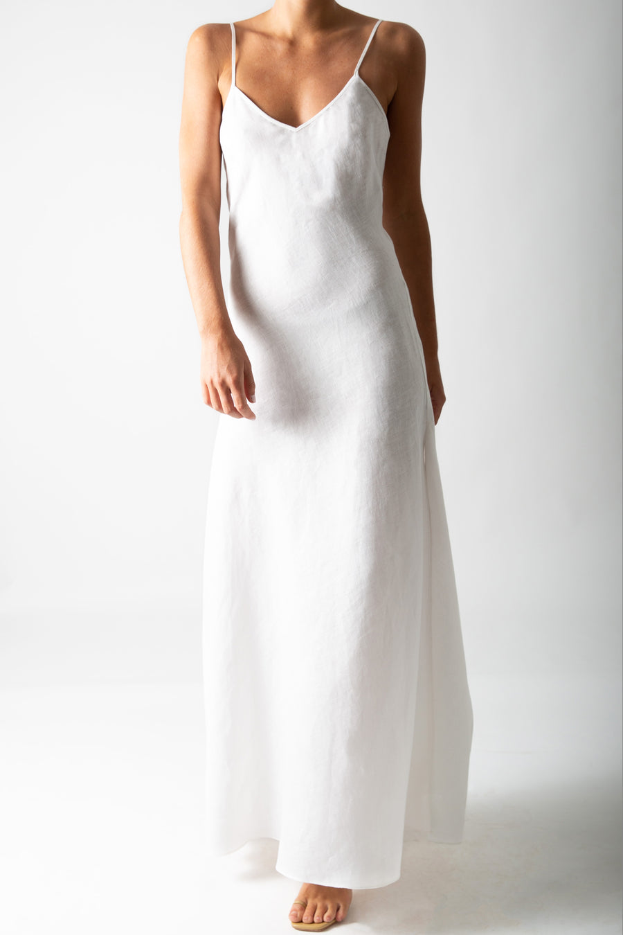 This is a photo of a woman from the neck down, she is wearing a white linen slip dress that reached to the floor.