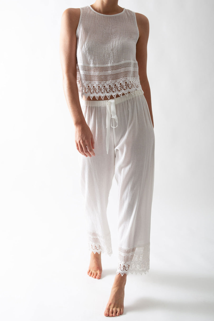 This is a photo of a woman wearing a white pair of pants with lace trim and matching white top with lace trim. The pants tie in the front.