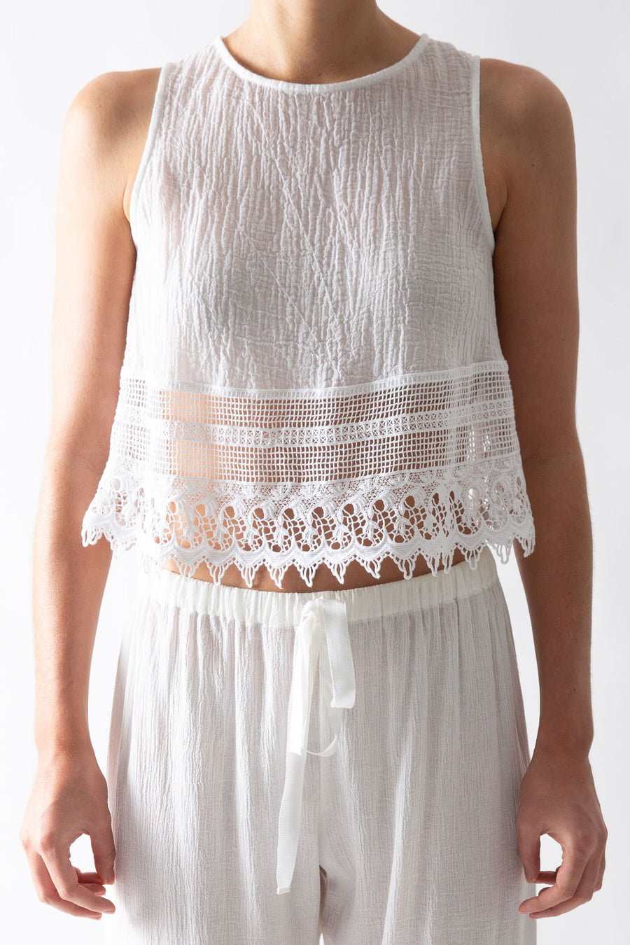 This is a detail photo of a cotton gauze white top with lace trim that meets the waistline of the pants.