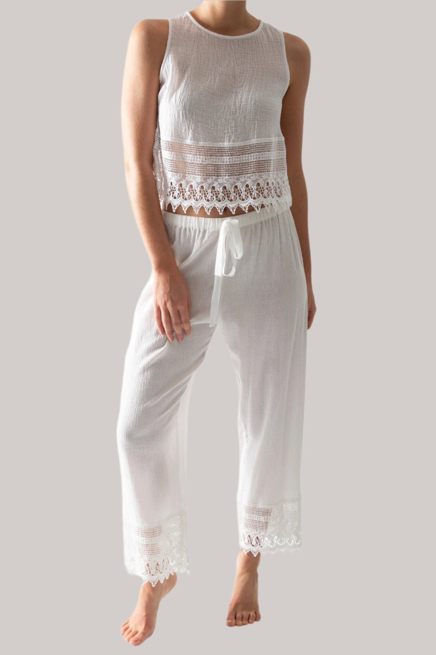 This is a photo of a woman wearing a white pair of pants with lace trim and matching white top with lace trim. The pants tie in the front.