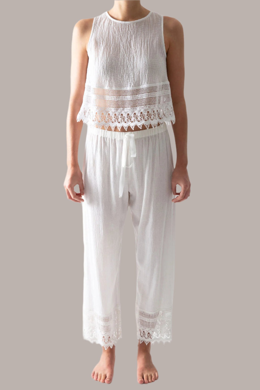 This is a photo of a woman wearing a white pair of pants with lace trim and matching white top with lace trim. The pants tie in the front.