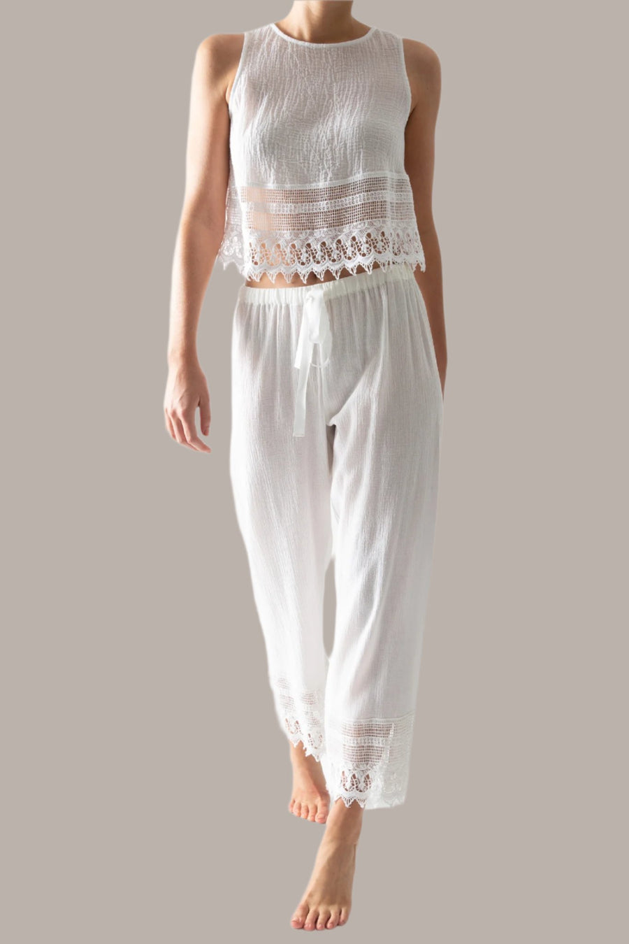 This is a photo of a woman wearing a white pair of pants with lace trim and matching white top with lace trim. The pants tie in the front.