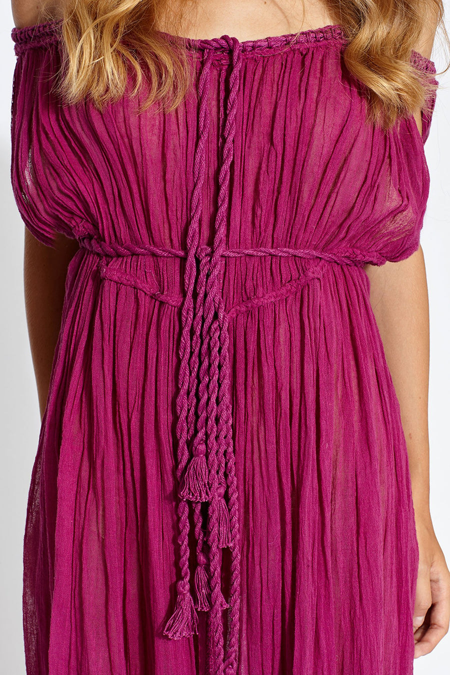 This is a detail photo of a magenta cotton gauze coverup dress with rope and tassel ties around center front and waist.