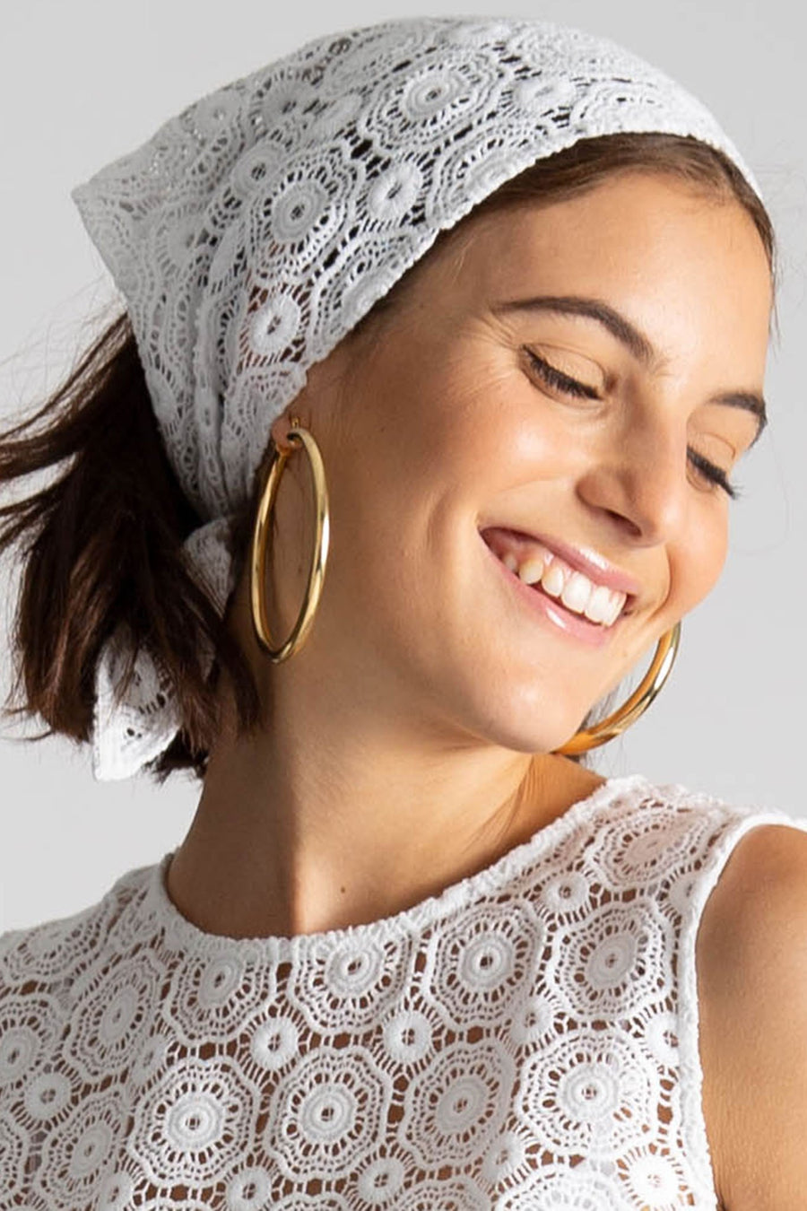 This is a photo of a girl wearing a lace headscarf with gold hoops and matching lace crop top. She smiles and looks over her shoulder.