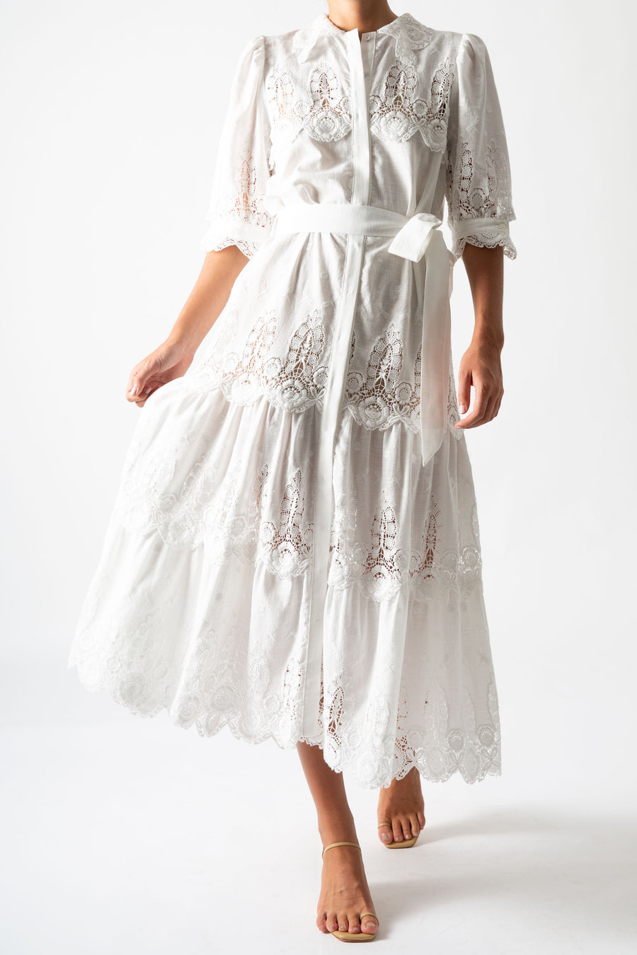 This is a photo of a woman wearing a long white linen and lace maxi dress with bow tie at the waist and puffy short sleeves.