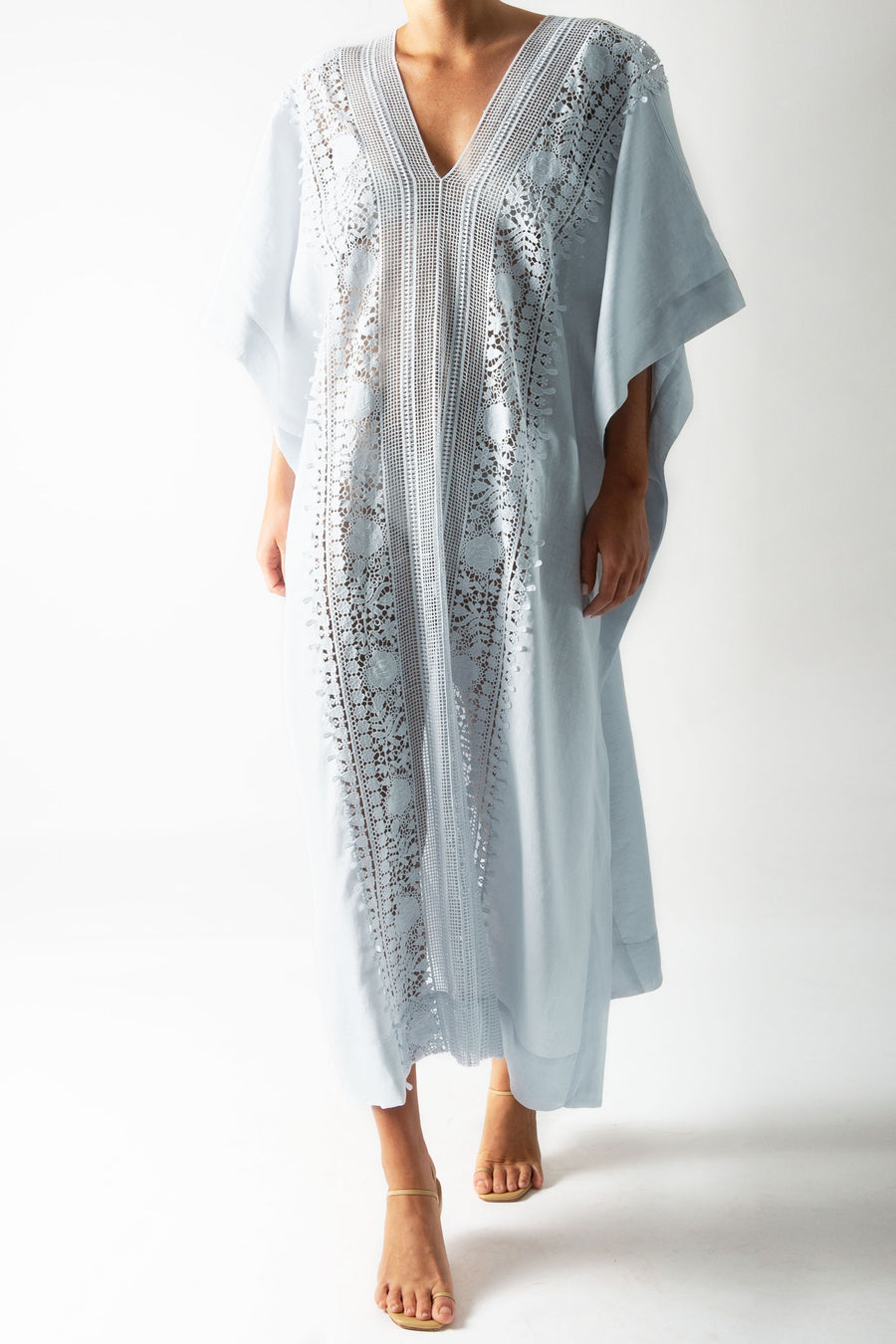 This is a photo of a woman wearing a light blue linen caftan with lace trim down the center.