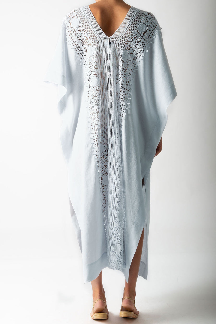 This is a photo of the back view of a woman wearing a light blue linen caftan with lace trim down the center.