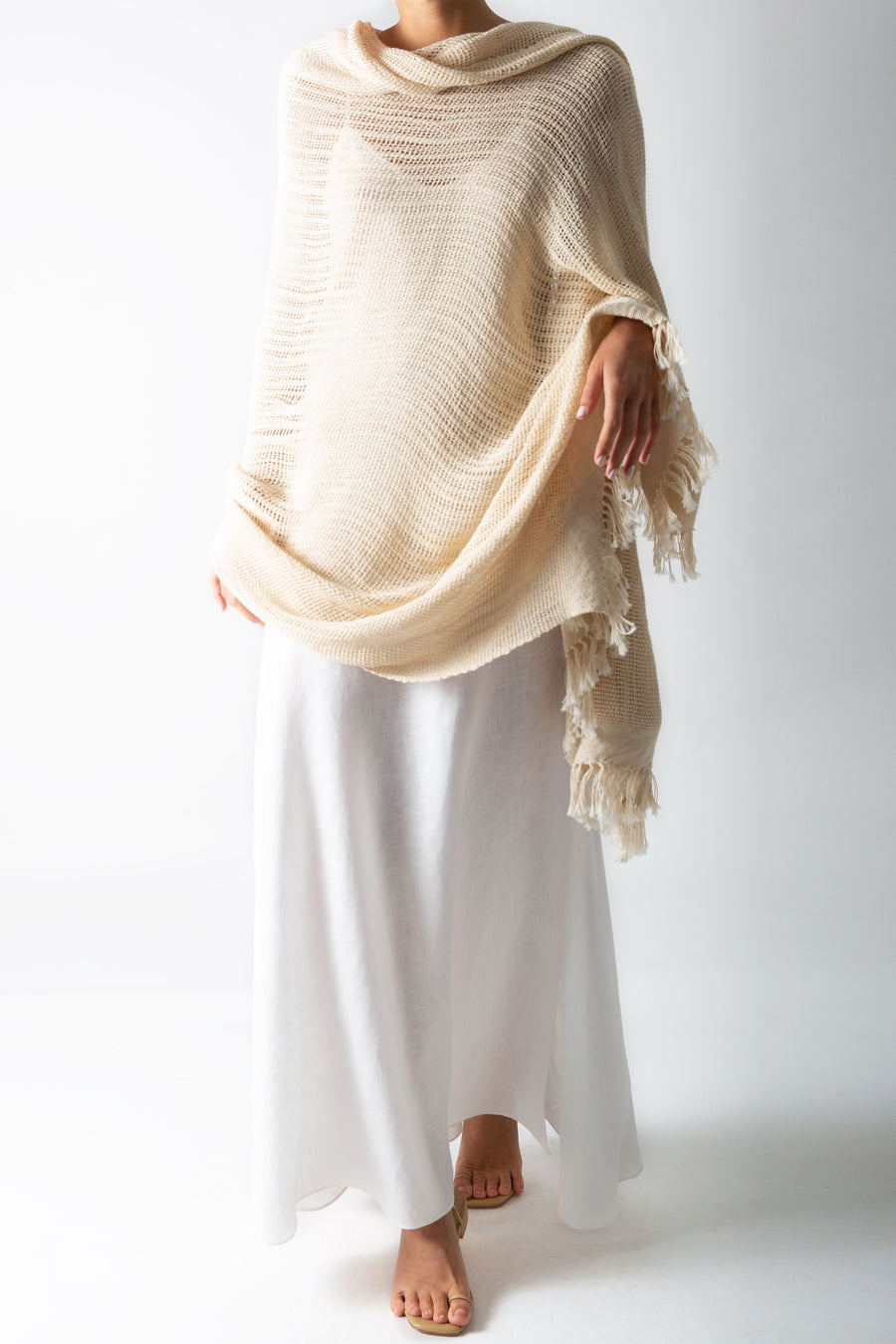 This is a photo of a woman wearing a white linen slip dress over a natural-colored shawl which is wrapped around her top half and arms.