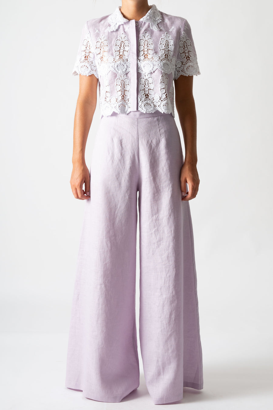 This is a photo of a women wearing a lavender cropped button down with white embroidery and lavander wide legged pants.