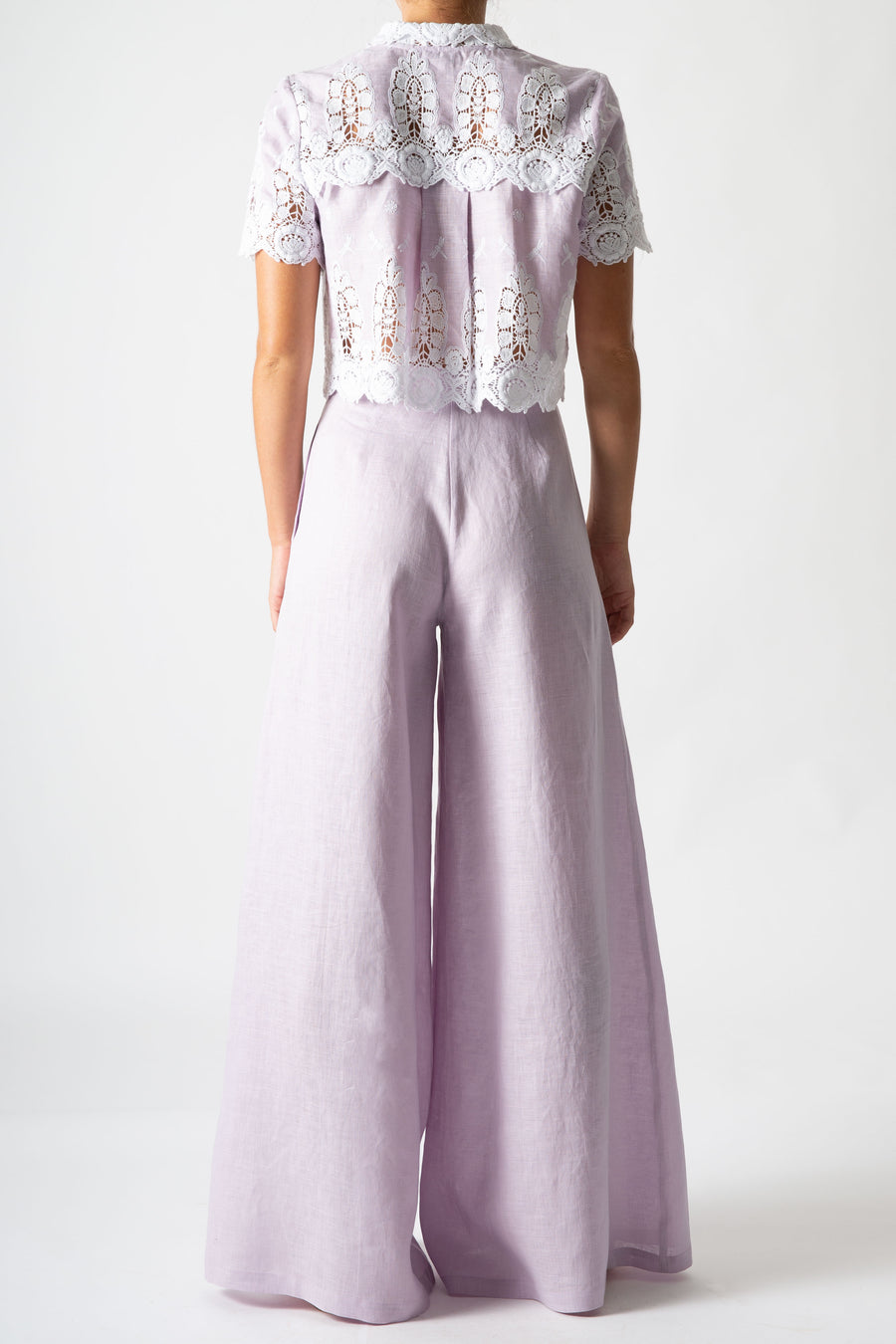 This is a back side photo of a woman wearing a lavander cropped button down with high-waisted lavander pants.