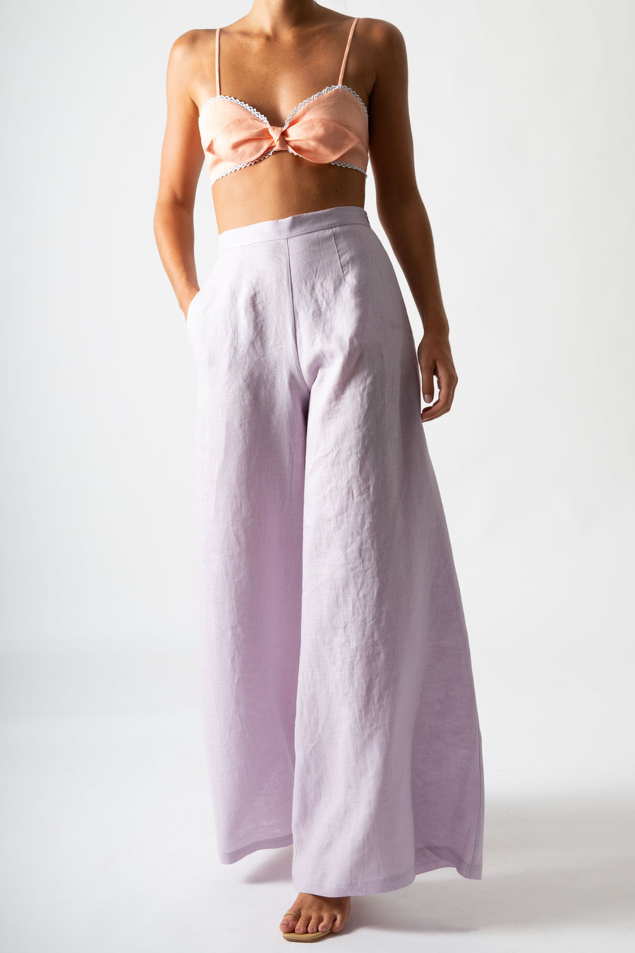 This is an image of a woman wearing a sorbet colored bralette with lavander wide legged pants.