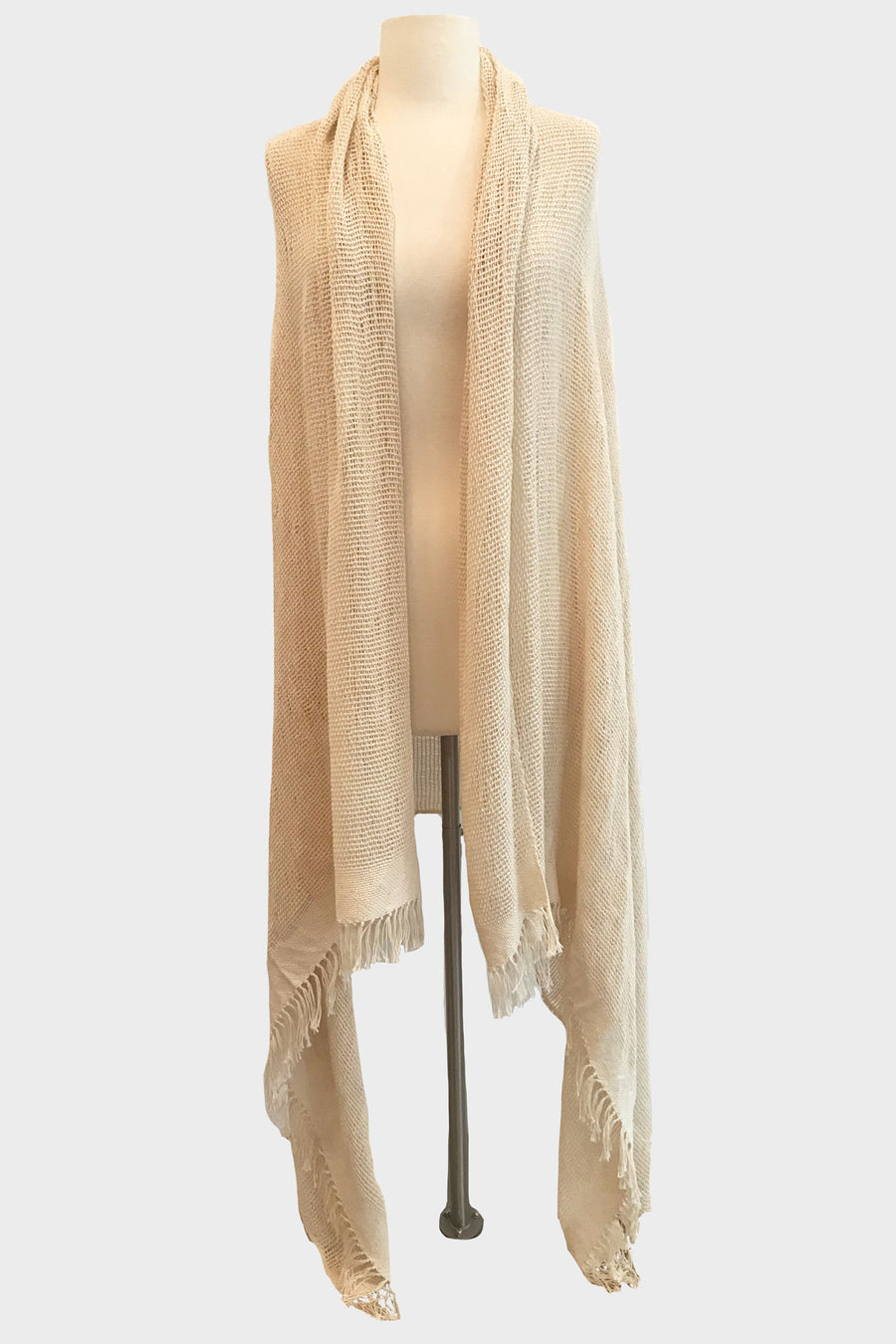 This is a photo of a natural-colored shawl on a mannequin. The shawl is open in the front and falls to the floor at the longest point.