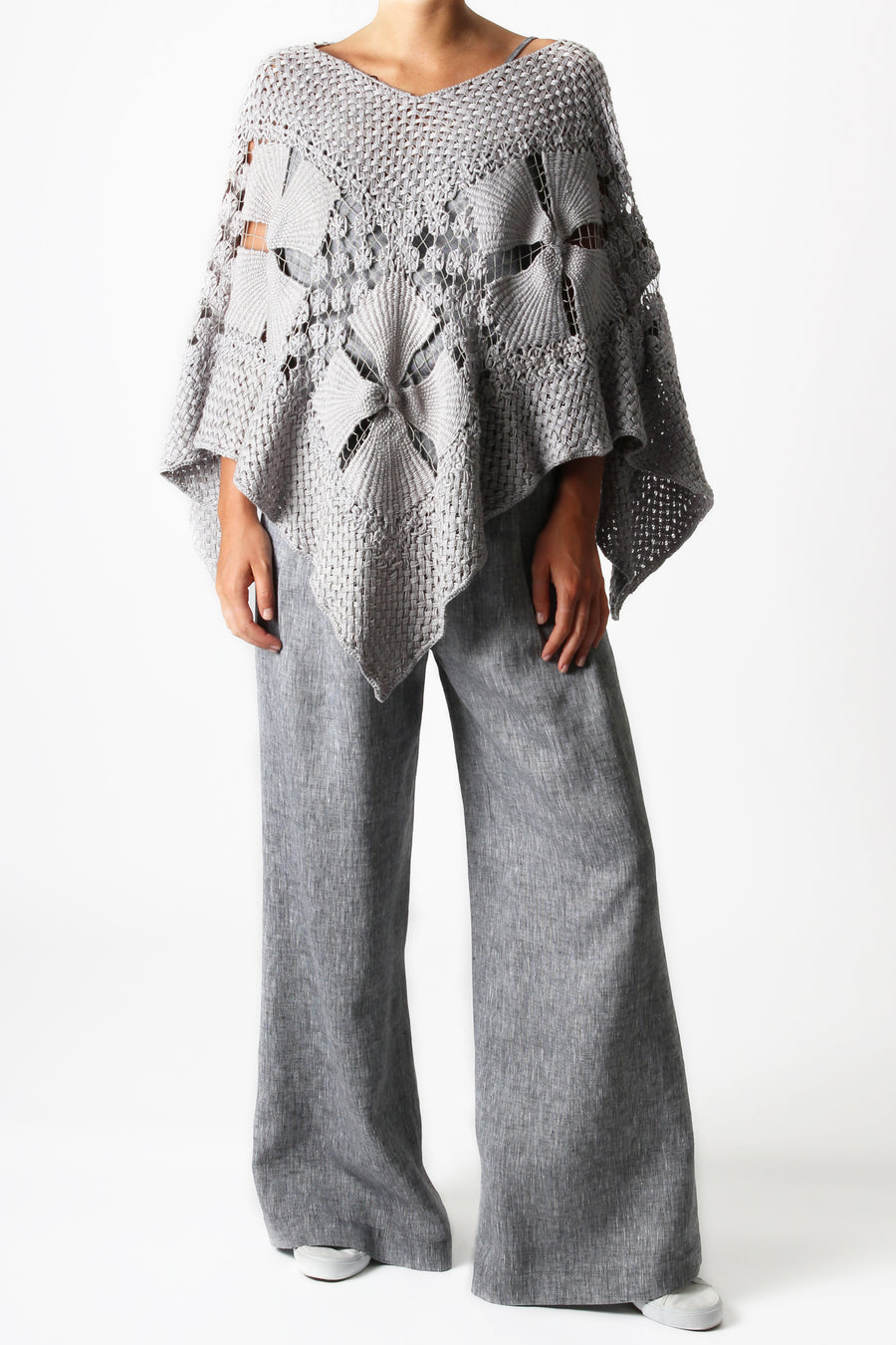 This is a photo of a woman wearing an all grey outfit with grey linen pants and a handmade grey knit shawl in the shape of a poncho.