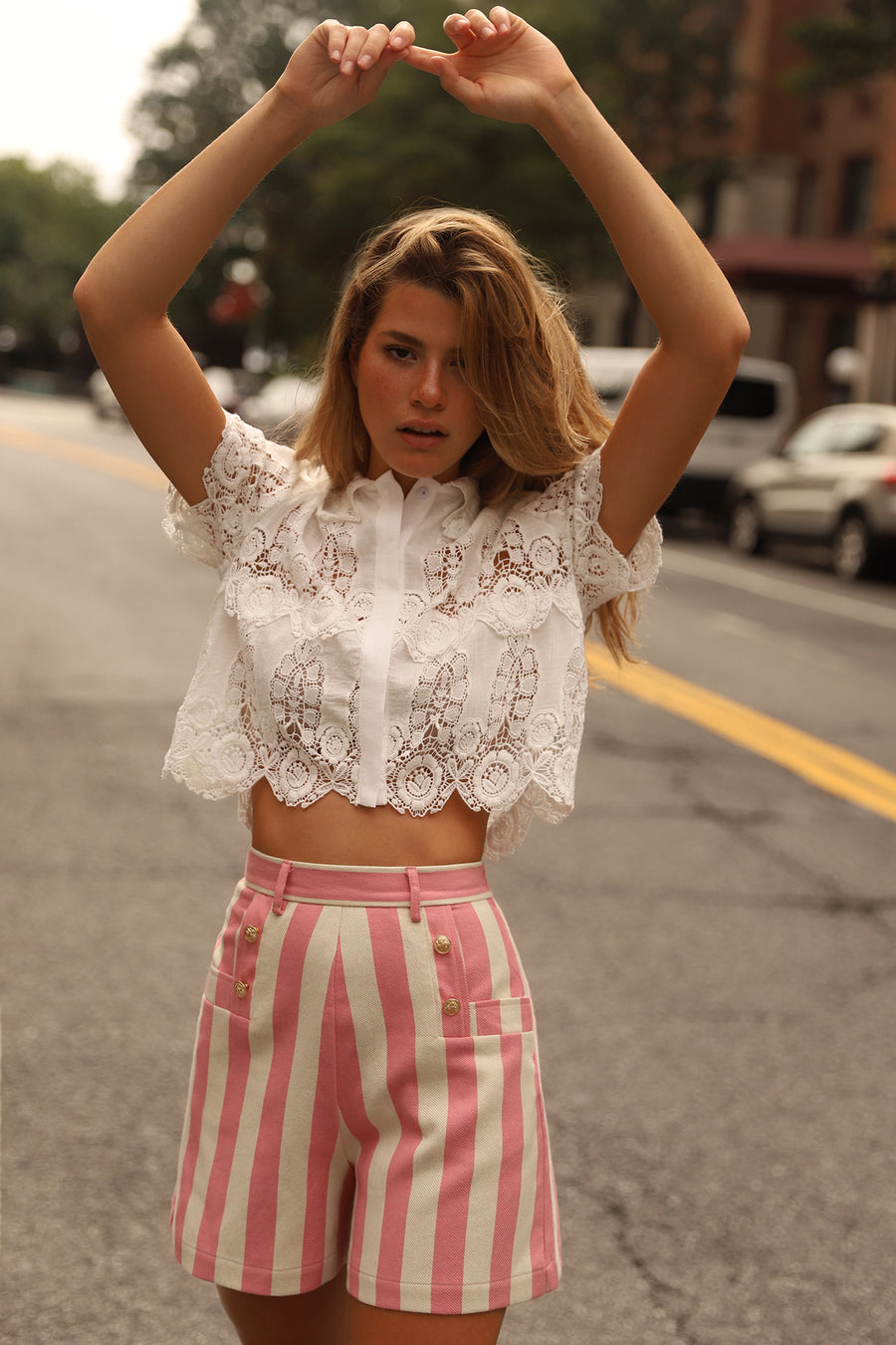 This is a photo of woman wearing a white lace crop top and pink striped shorts.