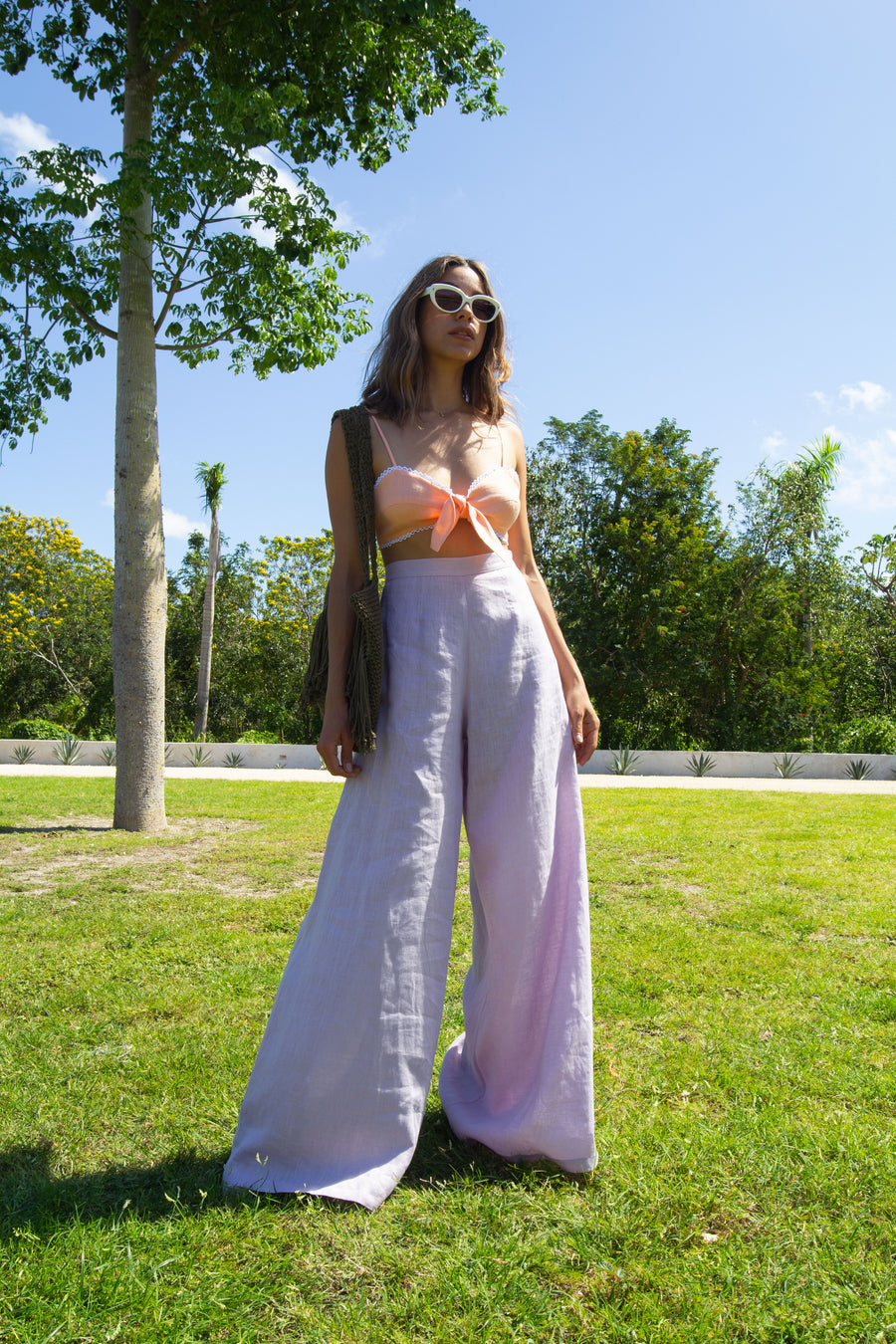 This is a photo of a woman wearing lavander wide legged linen pants with a sorbet colored bralette. 