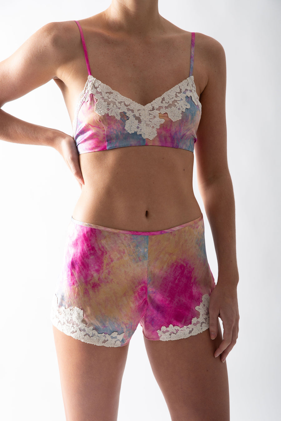 This is a photo of a woman wearing a tie dye silk set of mini shorts and bralette with lace trim.